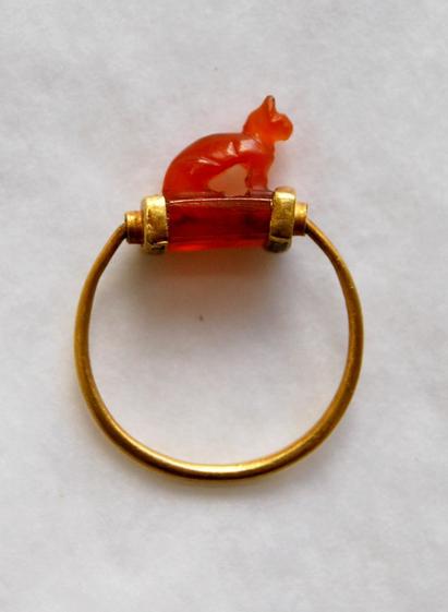 A gold ring with a red translucent gemstone featuring a small cat-shaped figure on top.