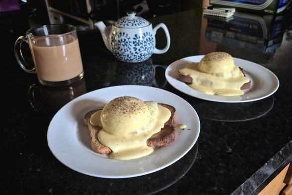 two dramatically lit plates of sorta eggs benedict, homemade bread with cararuby malt toasted, homemade beef/pork/lamb breakfast sausage topped with poached eggs and smothered in hollandaise and dusted with fresh ground pepper

a small teapot and a glass mug of tea with milk are in the background