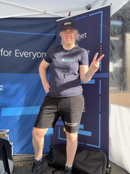 Slightly chubby white woman in knee long shorts, dark blue t-shirt and black caps - all Internet Society branded.