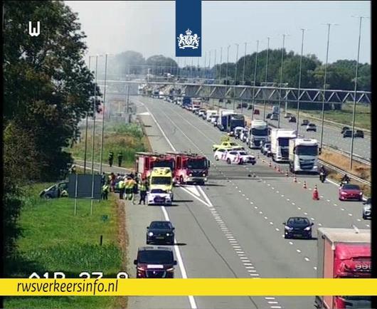 Verschillende hulpdiensten zijn aanwezig. Je ziet voertuigen van Rijkswaterstaat, politie, brandweer en ambulance. Een betrokken voertuig staat in de berm. Twee andere voertuigen staan op de vluchtstrook.