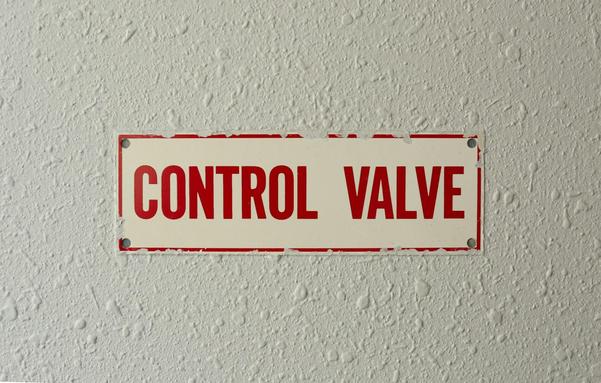 Red-and-white sign reading "CONTROL VALVE" mounted on a textured white wall to mark the location of a building control valve.