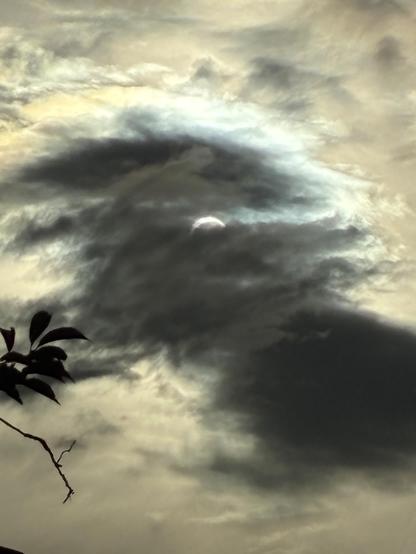 The sun, largely eclipsed by the moon, surrounded by dark swirls of cloud.