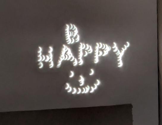 The words "B HAPPY" and a smiley face written with pinholes during the eclipse