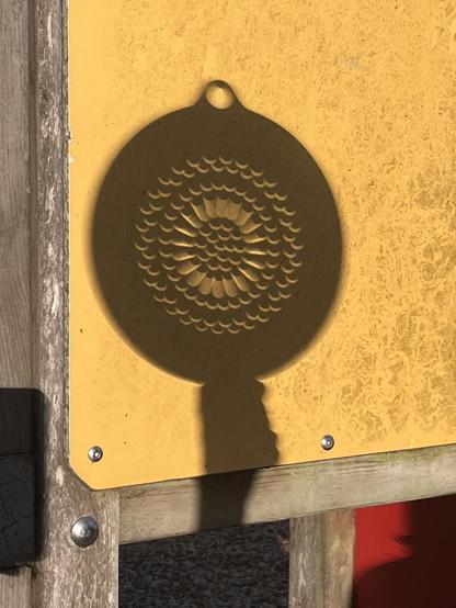 A yellow playground wall, with the solar eclipse projected through a colander. Every hole of the strainer is projecting a tiny crescent sun.