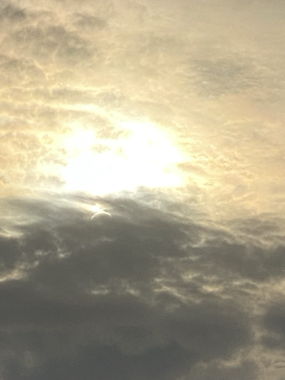 Sun lit clouds. In the grey clouds below, a crescent of the sun is visible shining through.