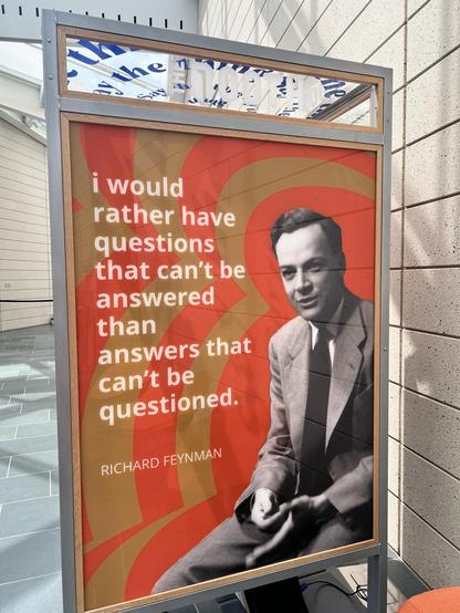 A poster featuring a black-and-white image of a man in a suit with a quote attributed to Richard Feynman: "I would rather have questions that can't be answered than answers that can't be questioned."