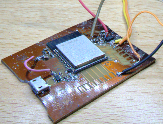 A circuit board with a smaller board soldered on in the center. The smaller board is covered with gray metal and says ESPRESSIF. Golden, and it has no solder mask. It's all scratched and with splotches of solder around. A resistor is standing on its side. There is a USB port and several free cables attached to spots on the other side. One soldered directly on another component.