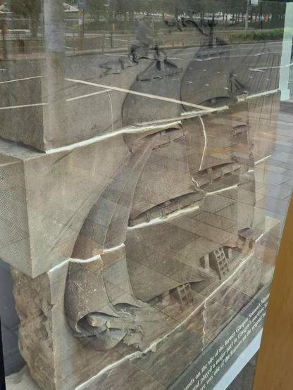 A sculpture of a sailing ship from an old building displayed int he window of the new one built in its place.
