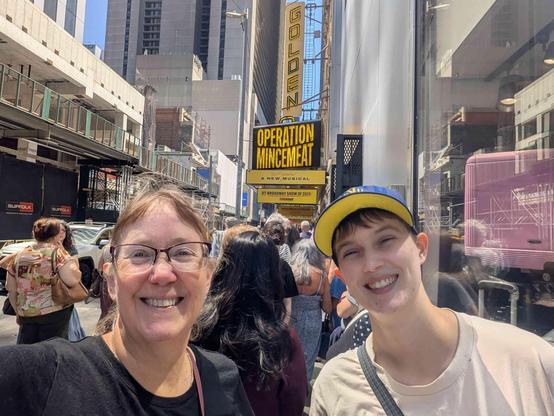 two happy people one on baseball cap standing in front of the theatre marque
