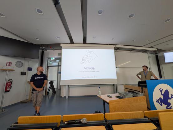 Lucas and Dirk on stage at FrosCon 2026 with a slide of the mosscap Logo in the middle.