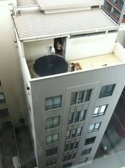 Three people setting up a trampoline on the small rooftop terrace of a tall building.