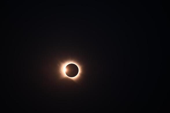 Foto des Beginns der totalen Phase der Sonnenfinsternis, links ist ein hell leuchtender Punkt und um den Mond sieht ma einen hellen Ring.