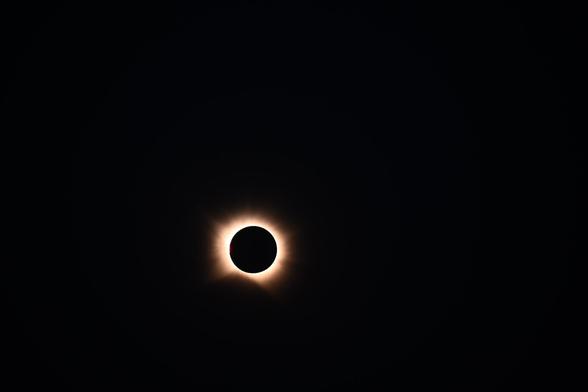 Foto der totalen Phase der Sonnenfinsternis, um den Mond sieht man einen hellen Ring mit unterschiedlich langen fransen.