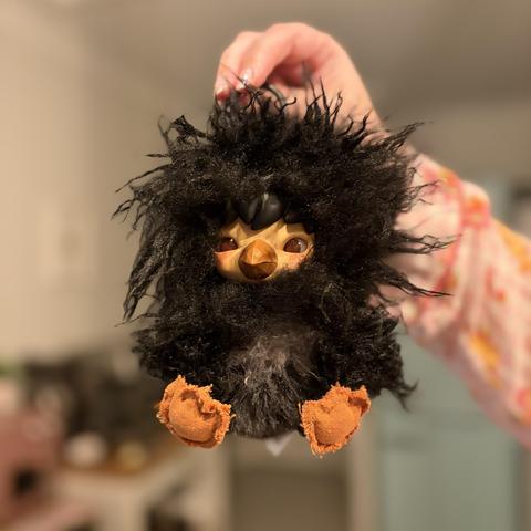 A small fluffy toy that looks like a bird with masses of uncontrollable black hair all over its body, dwarfing its face