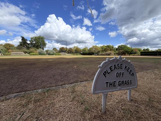 Please keep off the grass sign, with dead grass lawn behind it