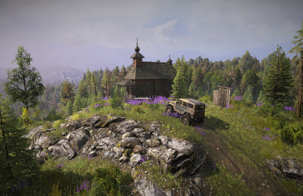 In-game screenshot of a rugged off-road SUV parked on a rocky outcrop near a small wooden Orthodox-style chapel with an onion dome, surrounded by wildflowers and pine forest with misty mountains in the background.