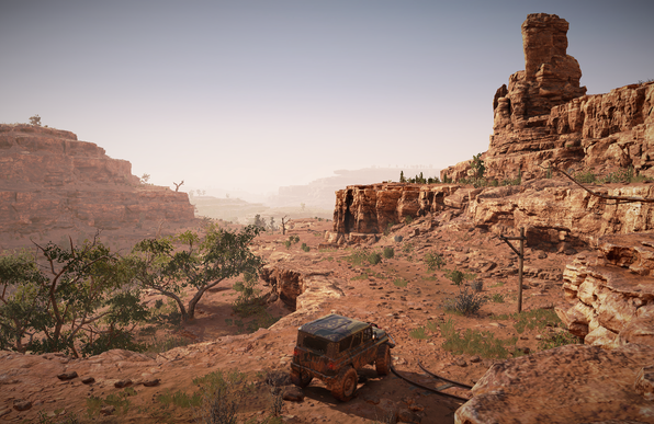 In-game screenshot of an off-road truck driving through a sun-drenched desert canyon lined with sandstone cliffs and towering rock formations, with a hazy valley stretching into the distance.