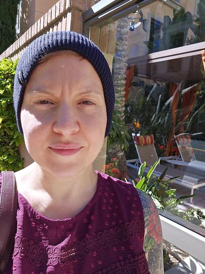 Photo of Ashley wearing a beanie and a maroon tunic in the sun beside a poolside cabana at Santa Clara Square in Santa Clara