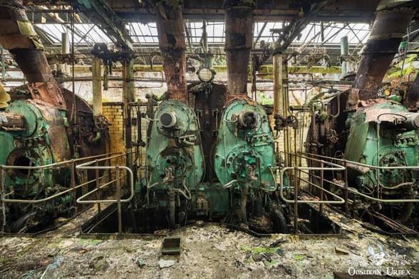 An abandoned industrial interior features large, rusted green machinery under a collapsing glass roof.