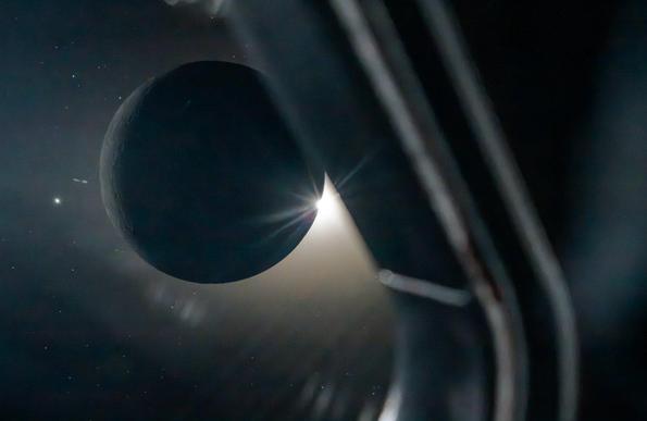 photo from the Artemis II mission, looking through the window of the ship at the moon, back lit by the sun, side lit by earth glow. the moon seems to be a ball just floating in space