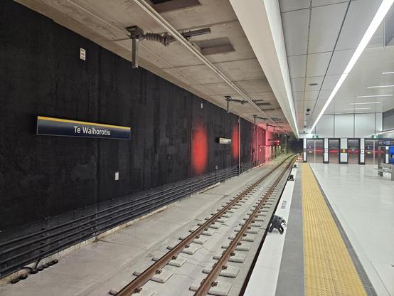 Looking at end of platform as the train tunnel heads out of the station. On the wall is station signage: "Te Waihorotiu"