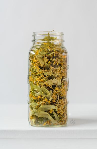 On a white backdrop, a large mason jar stuffed with  green and yellow-green dried herb.