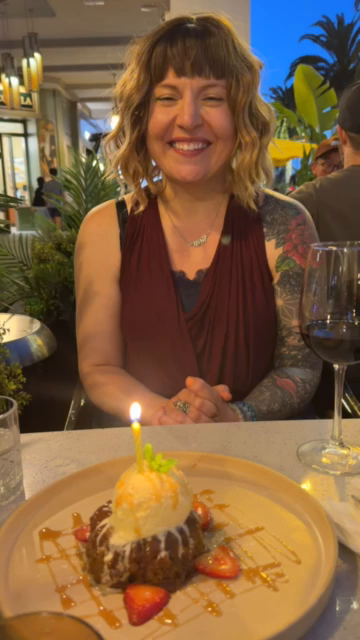 video of Ashley blowing out the candle on a cake while sitting at an outdoor patio table at Santana Row in San Jose