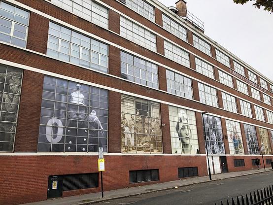A red brick building features large, historical black-and-white murals displayed on its windows. The images depict various figures, including a police officer, part of the Metropolitan Archive.