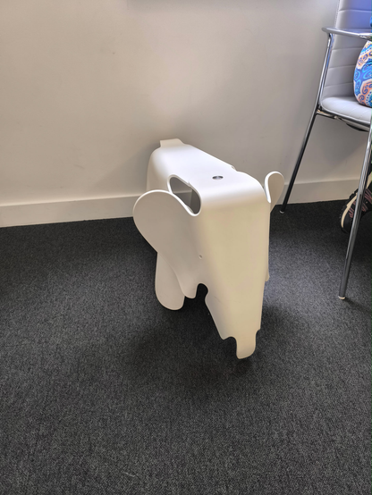 A small white elephant stool, about chair height. It has white ears that stick out for someone to play with and/or hold onto.