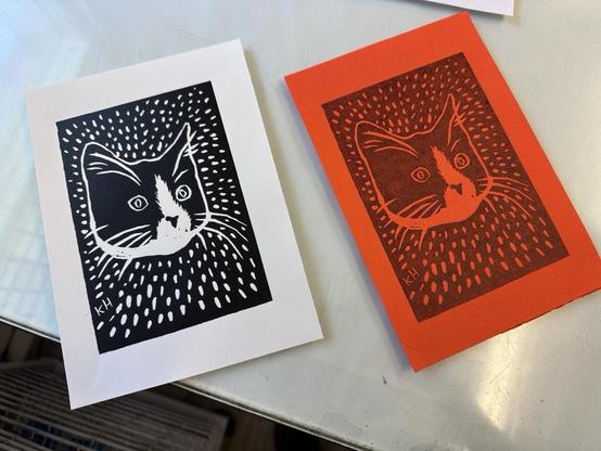 Two prints of a cat printed in black ink on white and orange paper