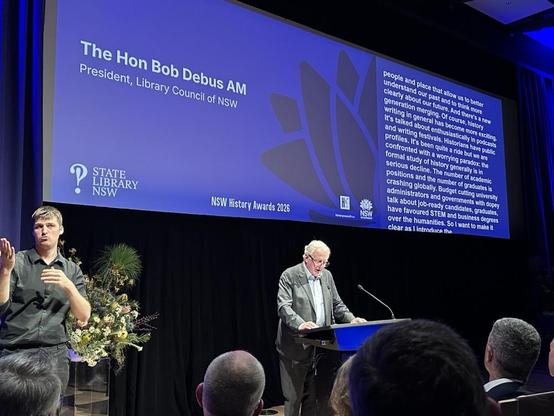 A man presenting to an audience from behind a lectern
