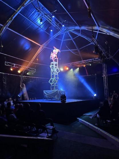 An acrobat doing a handstand on a precariously balanced tower of chairs on top of a table