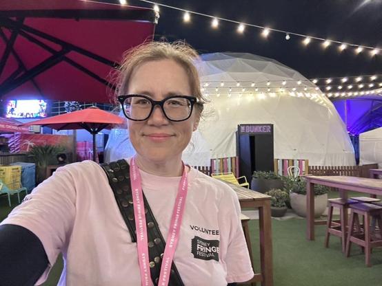 A woman in a pink shirt and lanyard standing outside a white geodesic tent