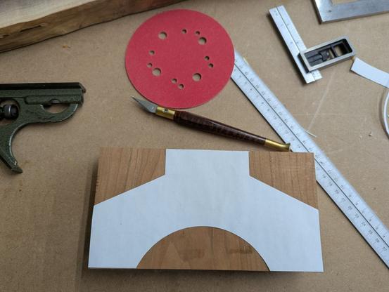 A work bench with a paper template on top on a cherry block with some tools like a ruler, marking knife, ruler, and square scattered about.