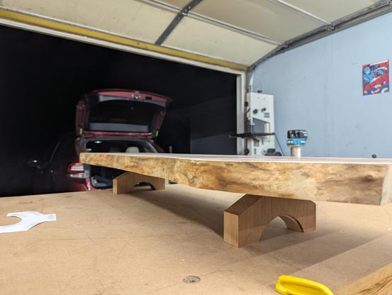 A walnut slab is sitting on top of the legs from the previous photo with an open garage door in the background.
