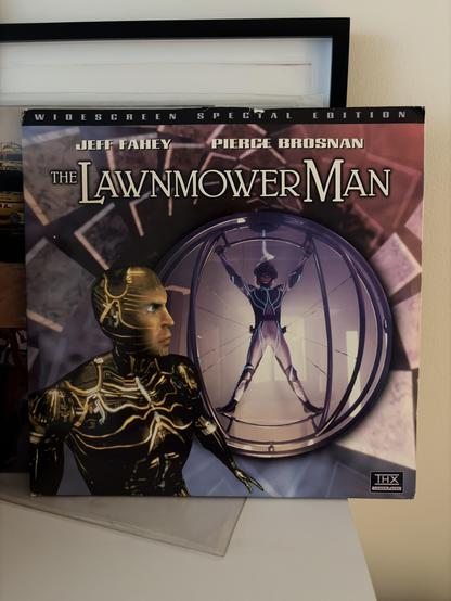 Cover of the movie "The Lawnmower Man" with images of a man with a cybernetic body and a woman in a futuristic suit inside a spherical structure.