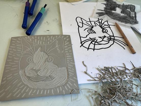 A linoleum block with a carved image of a cat on it, next to a printed image of the cat