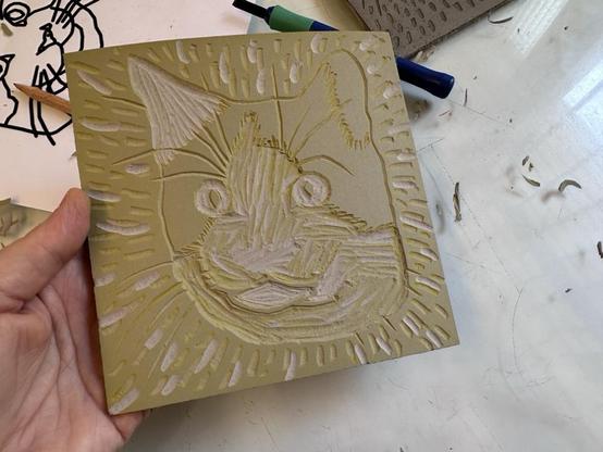A cat carved into a linoleum block, which is stained yellow from a previous inking.