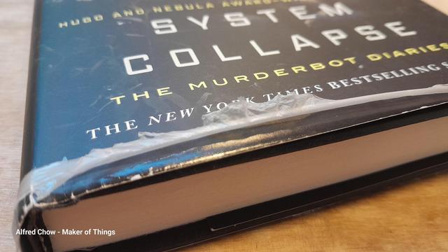 The bottom edge of a hardback book (Martha Wells- System Collapse).
The film on the paper dust cover has peeled away along the edge and looks really messy and horrible, like scabby peeling skin!