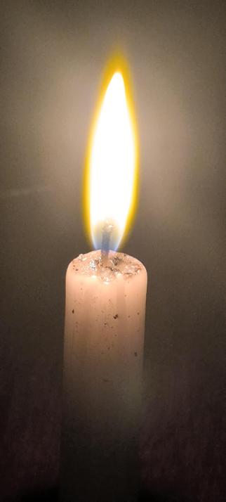A close up of a candle flame, with some dark spots on the molten part of the wax showing burnt salt.