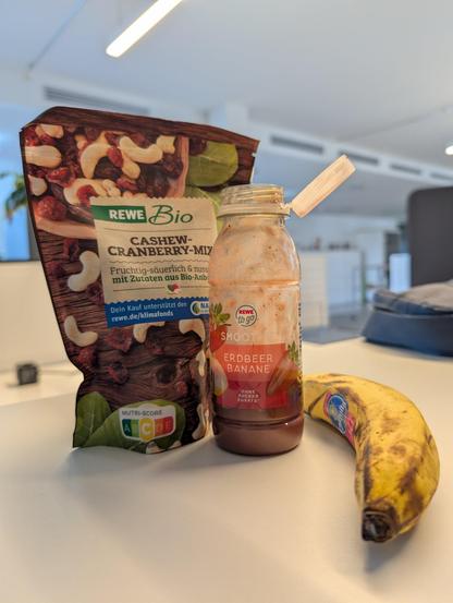 Cashew cranberry mix packet with banana strawberry smoothie and a banana sitting on the table.