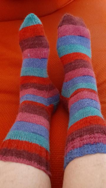 A pair of feet in striped hand knit socks in people, blue green and red. Some mistakes were made, but nothing i can't live with. Also, one of them is slightly longer than the other.