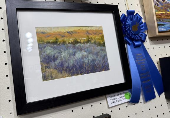 A framed pastel painting titled "Sunset over the City". There's a blue ribbon on the side. It won the first place in pastel division.