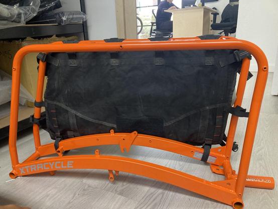 What you literally see is sort of a narrow box frame, painted orange. It's a frame that you add on to the rear of a bike to extend it and make it into a long-tail cargo bike