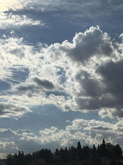 Blue sky with backlit clouds over a tree line.
