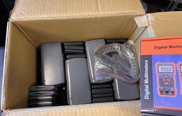 Box of the calculators stacked efficiently. Also a bag of some of the transparent style protractors, and an example of the multimeters in its original box.