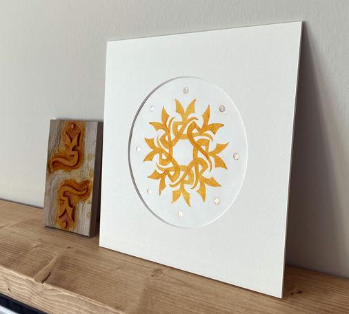 The same print shown propped up on a wooden shelf, the woodblock plate beside it.