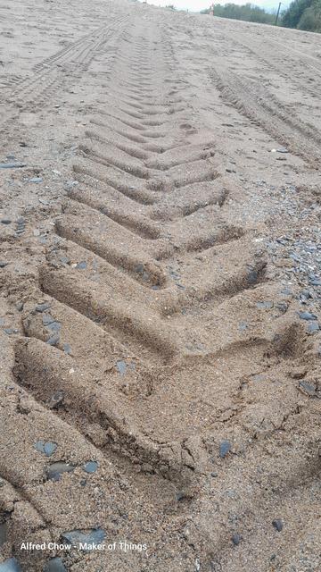 The imprint of a big tractor tyre in the sand.  The view is low down looking along the tread pattern as it disappears over the sandy horizon of the beach.