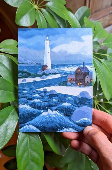 Photo of a hand holding a postcard showing a lighthouse and some houses on two headlands. The sea is rough and the sky is full of storm-clouds.