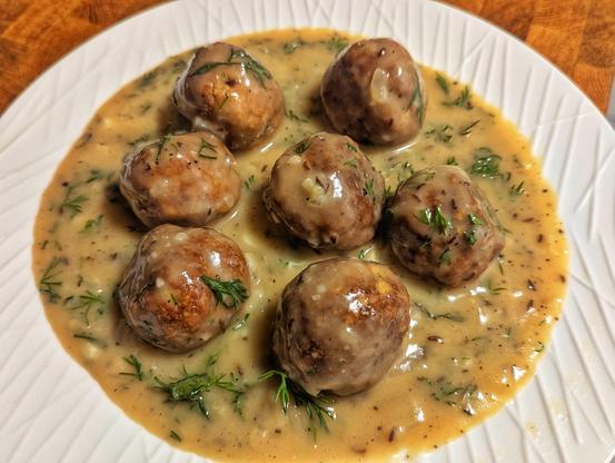Seven vegan 'meatballs' soaked on gravy made vegan sourcream and caraway, topped with dill.